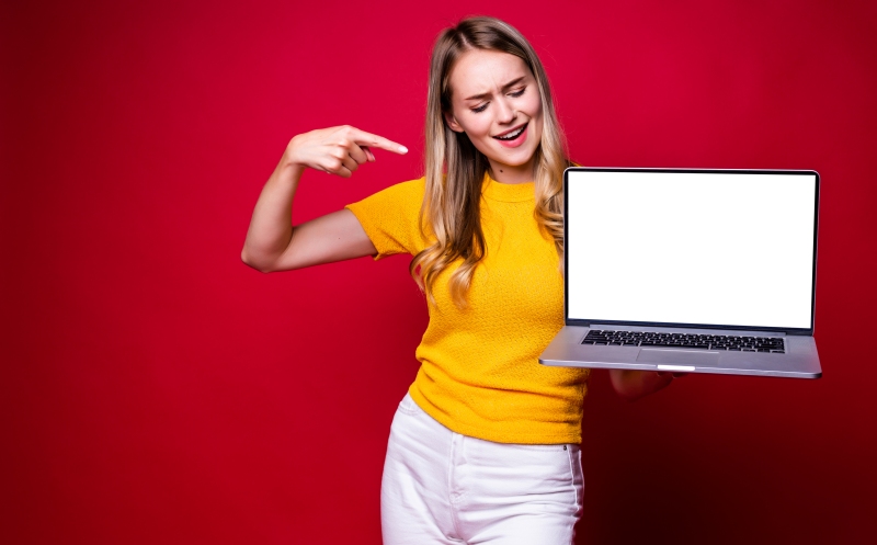 Portrait of young woman holding, working on laptop pc computer isolated on red background.